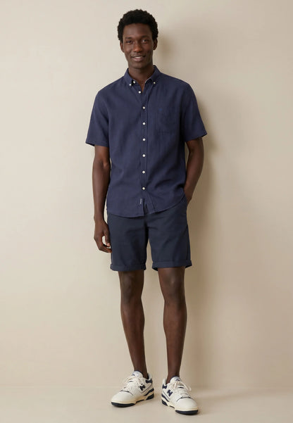 Man wearing a navy shirt and shorts with white sneakers against a beige background