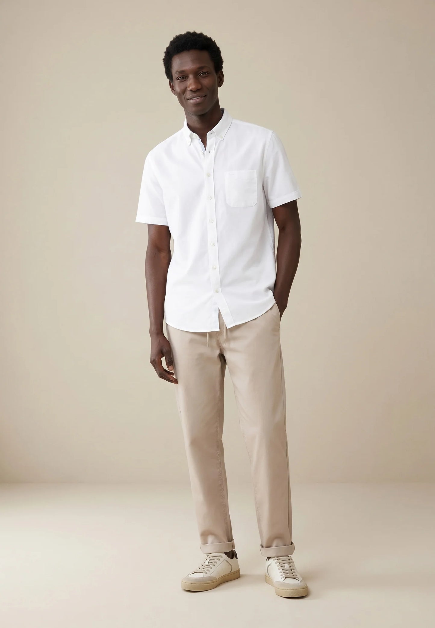 Man wearing a white shirt and beige pants against a beige background