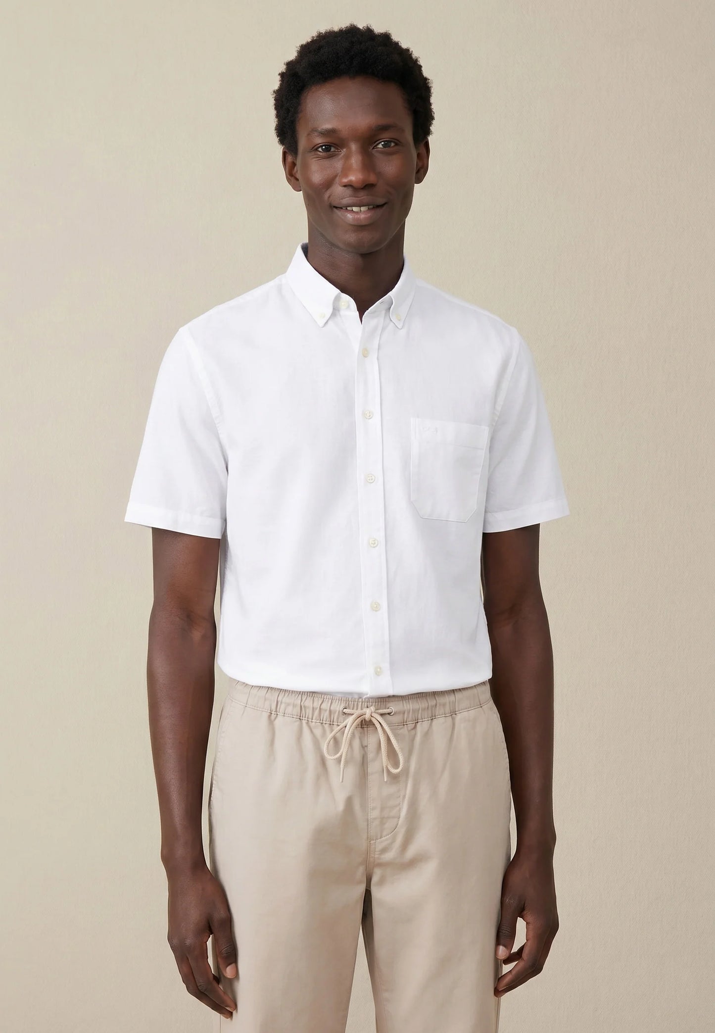 Man wearing a white short-sleeve shirt and beige pants against a beige background