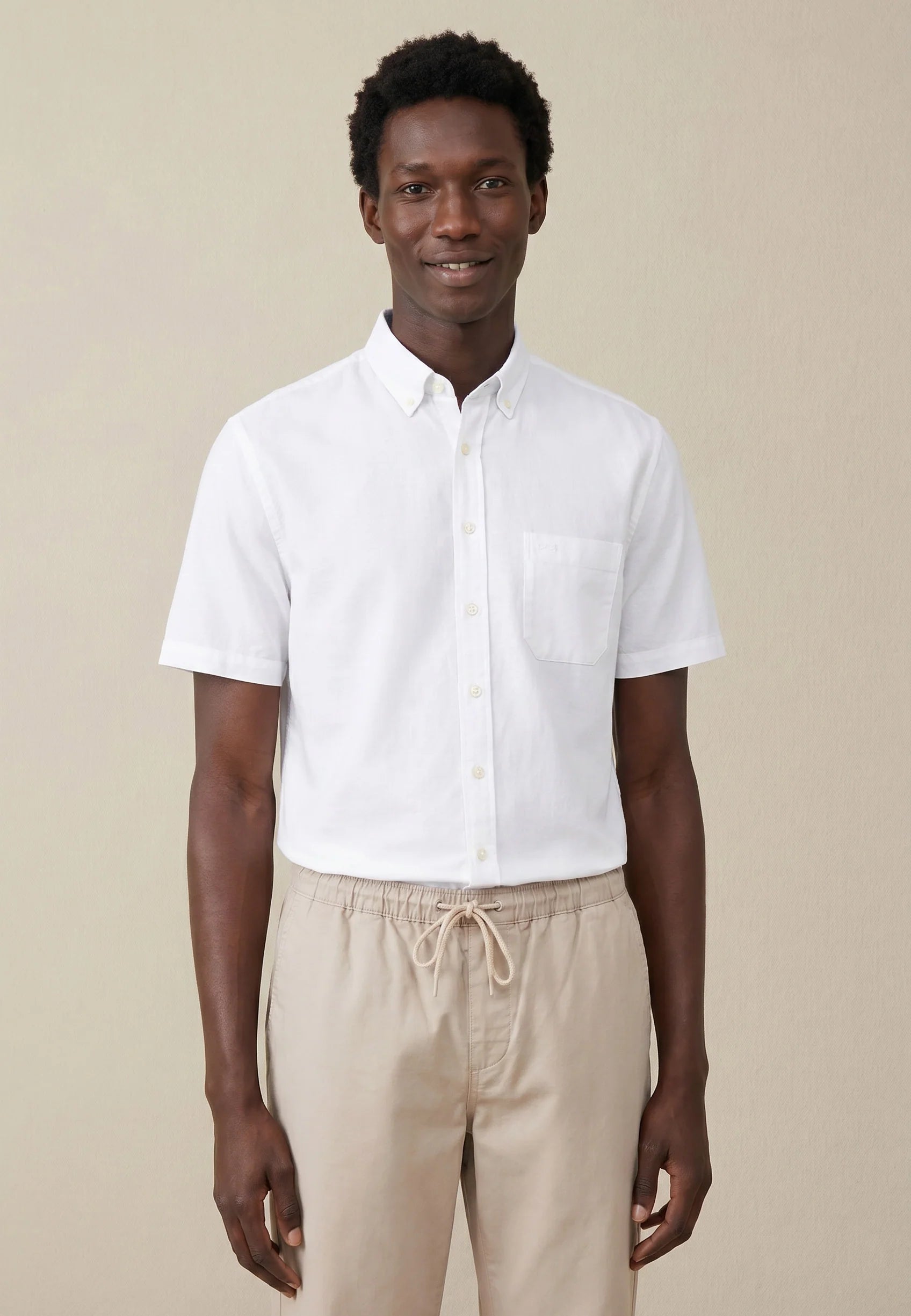 Man wearing a white short-sleeve shirt and beige pants against a beige background