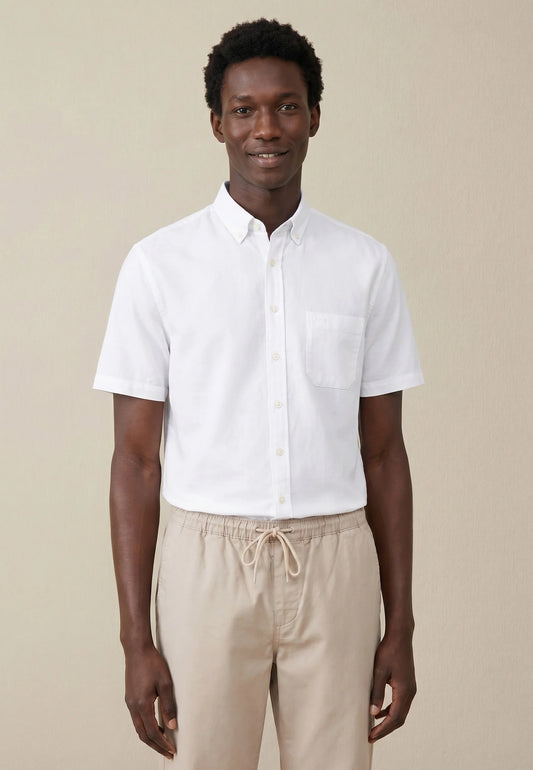 Man wearing a white short-sleeve shirt and beige pants against a beige background
