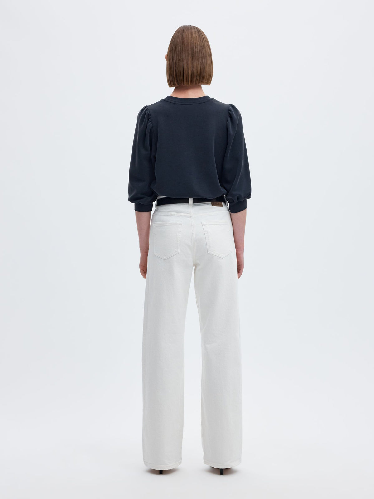 A model shown from the back wearing a dark navy long-sleeve top with puffed shoulders and white wide-leg trousers, against a plain white studio background.