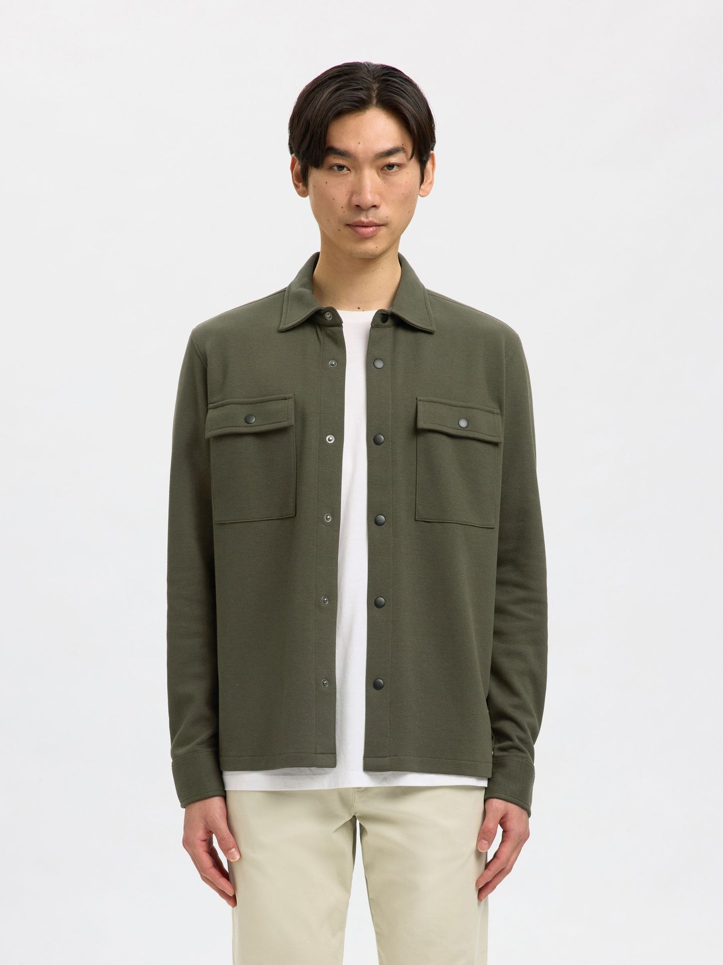 Man wearing a green jacket over a white shirt on a light gray background