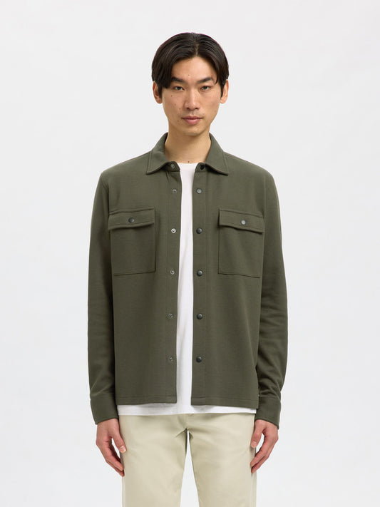 Man wearing a green jacket over a white shirt on a light gray background