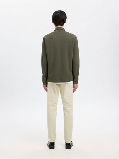 Person wearing a green long-sleeve shirt and beige pants on a white background