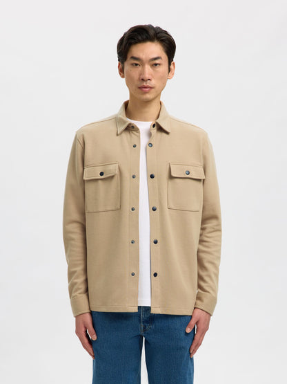 Man wearing a beige jacket over a white shirt on a light gray background