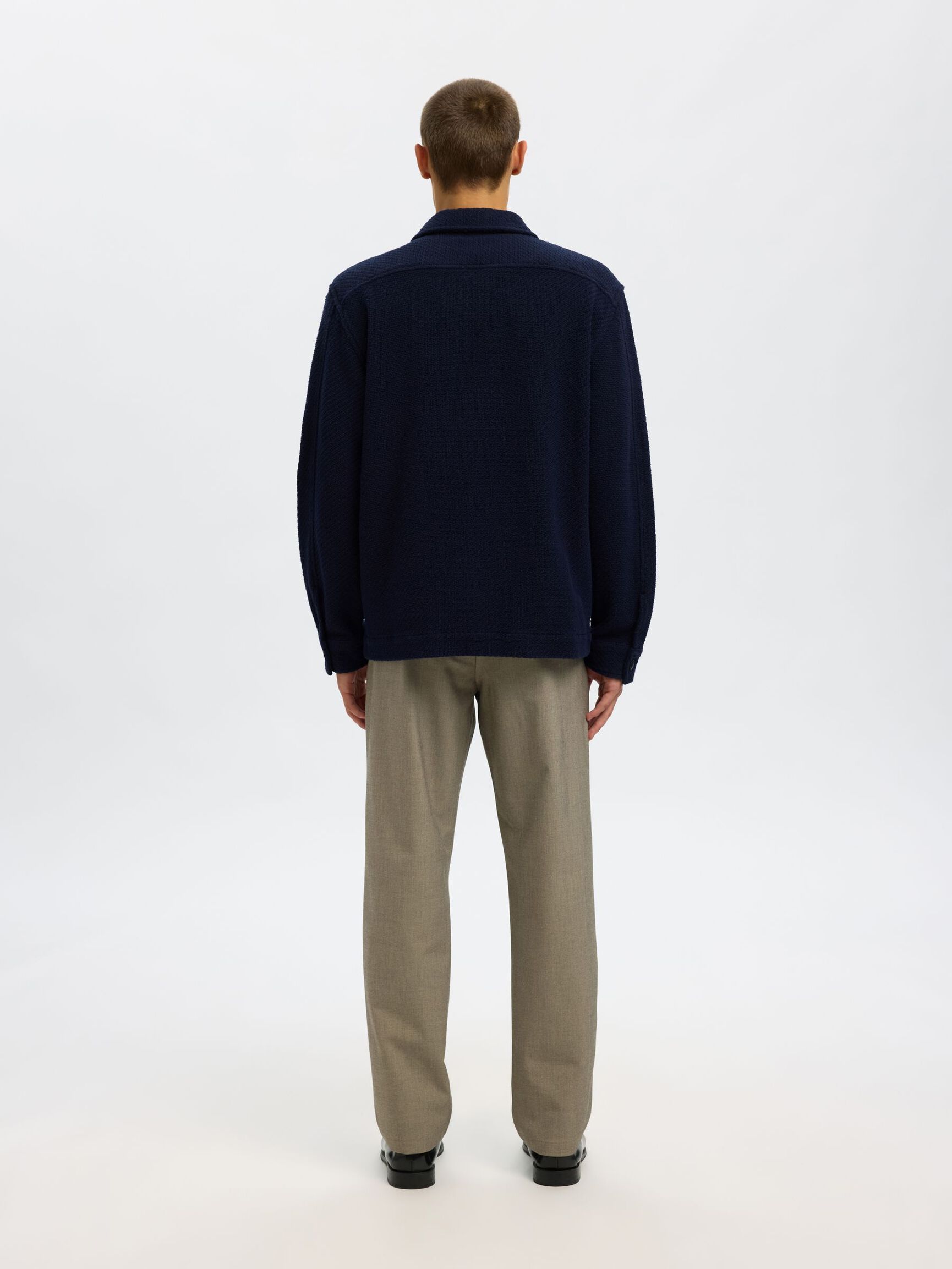 Person wearing a navy sweater and beige pants on a white background
