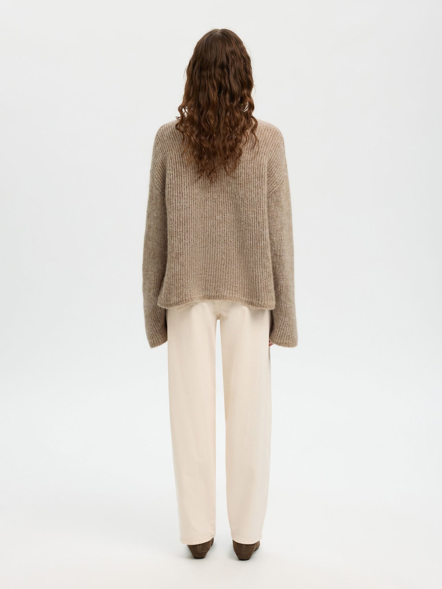Person wearing a beige sweater and white pants on a white background