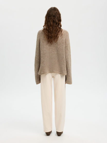 Person wearing a beige sweater and white pants on a white background