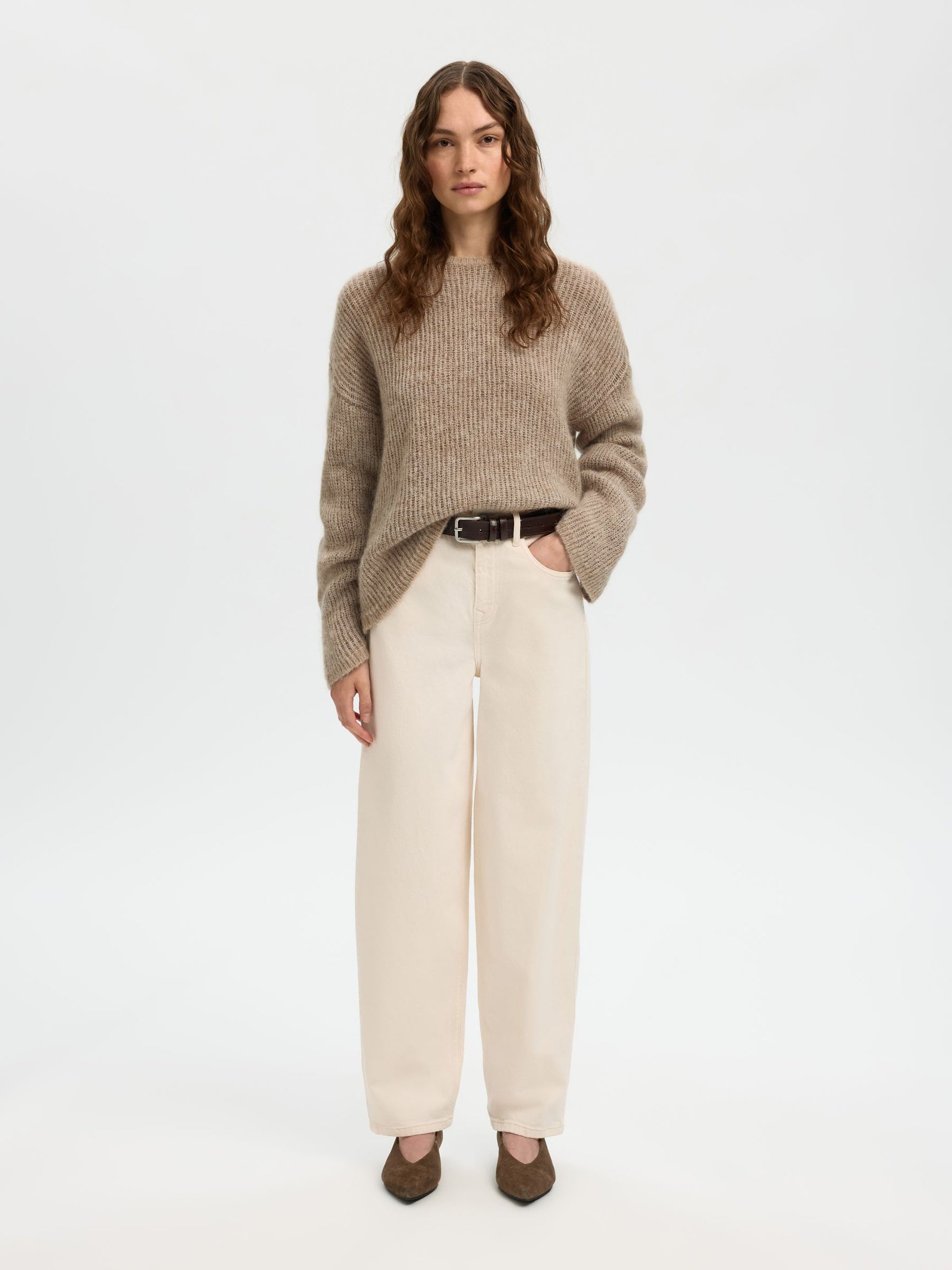 Woman wearing a beige sweater and cream pants on a white background