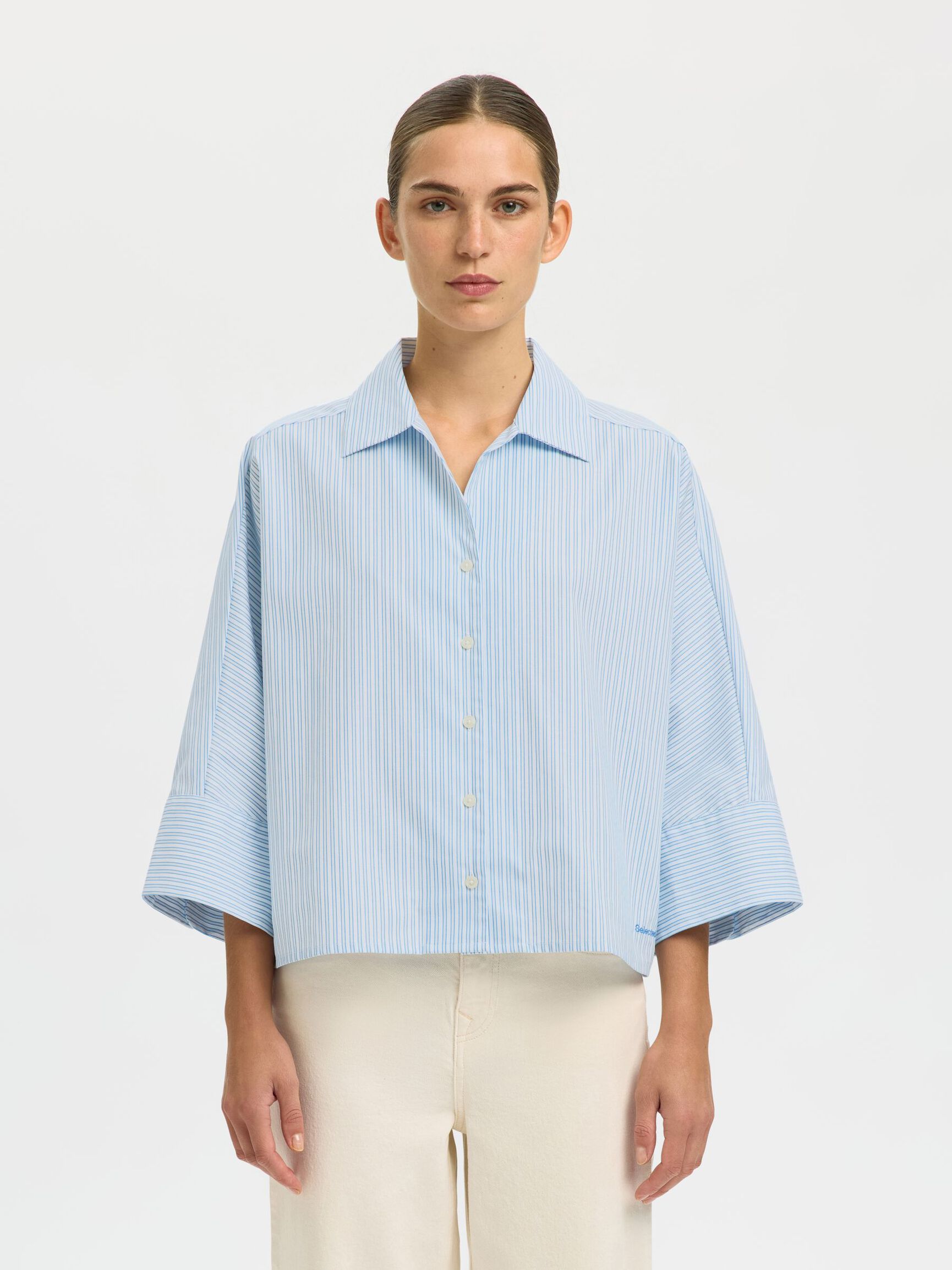 Woman wearing a light blue striped shirt against a white background