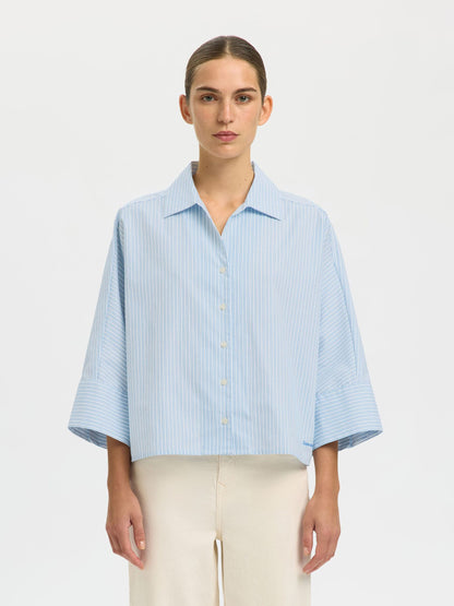 Woman wearing a light blue striped shirt against a white background