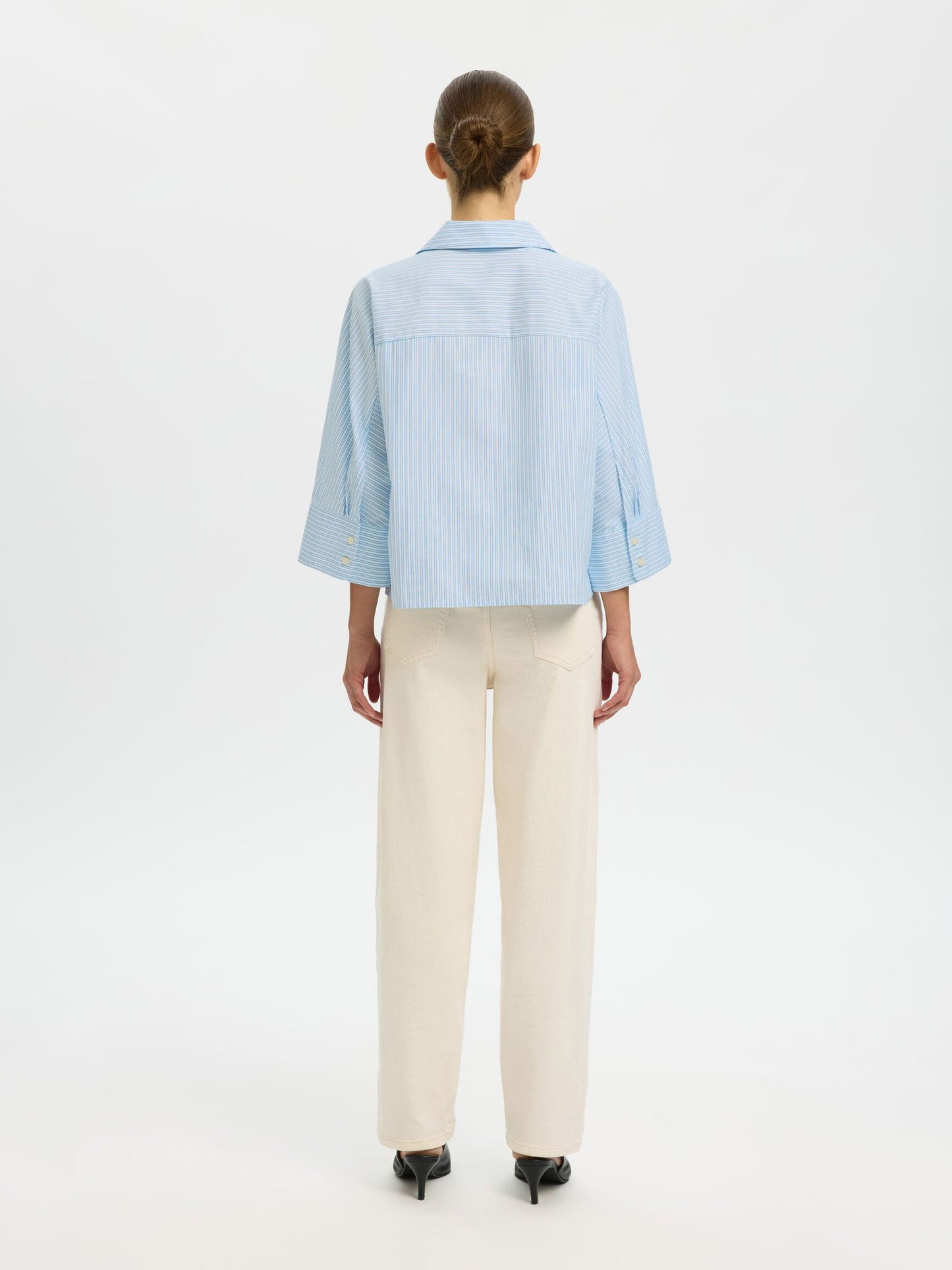 Person wearing a light blue shirt and beige pants on a white background