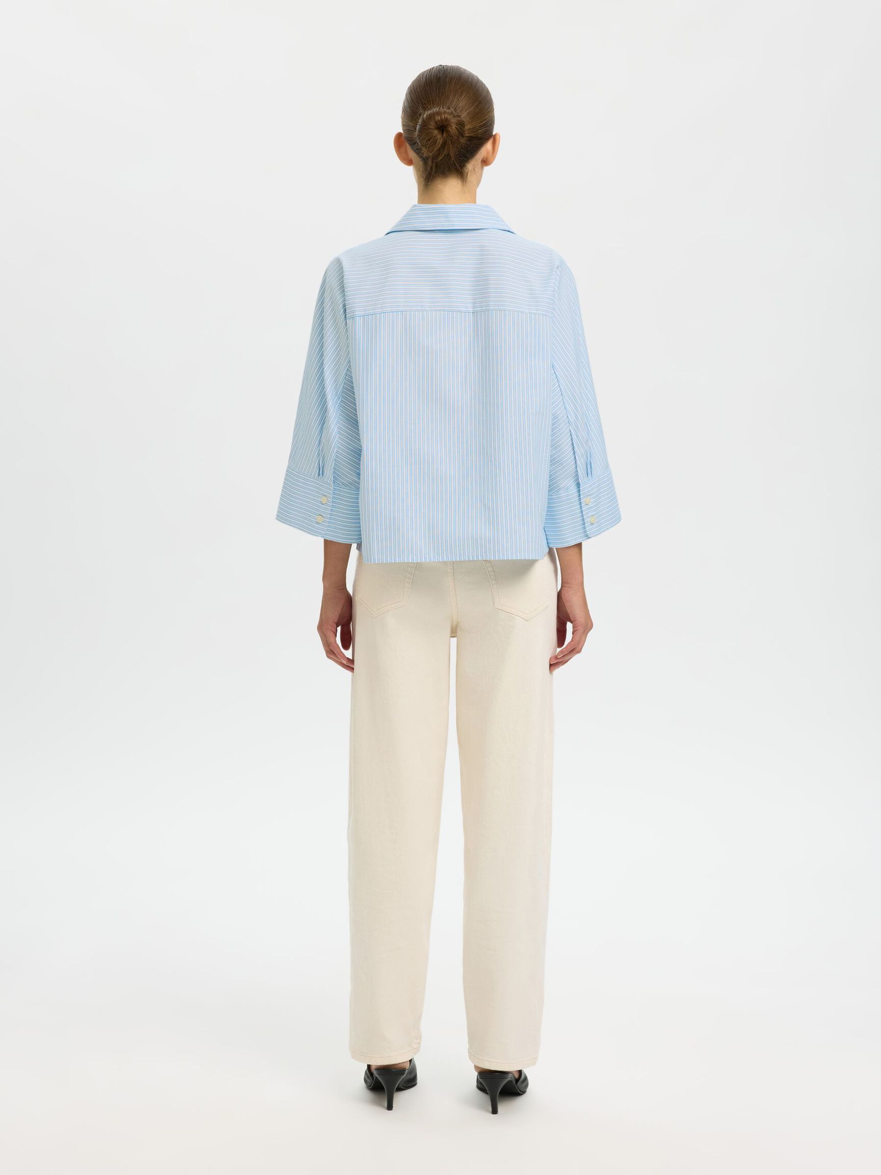 Person wearing a light blue shirt and beige pants on a white background