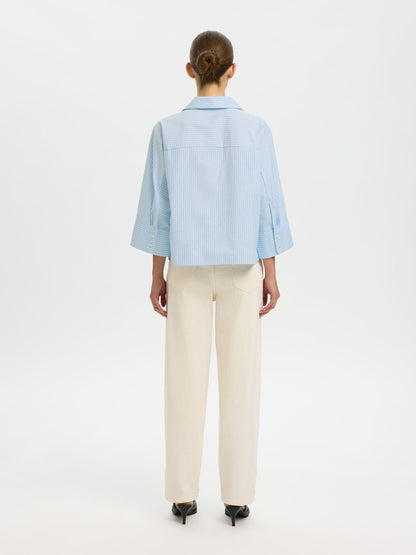 Person wearing a light blue shirt and beige pants on a white background