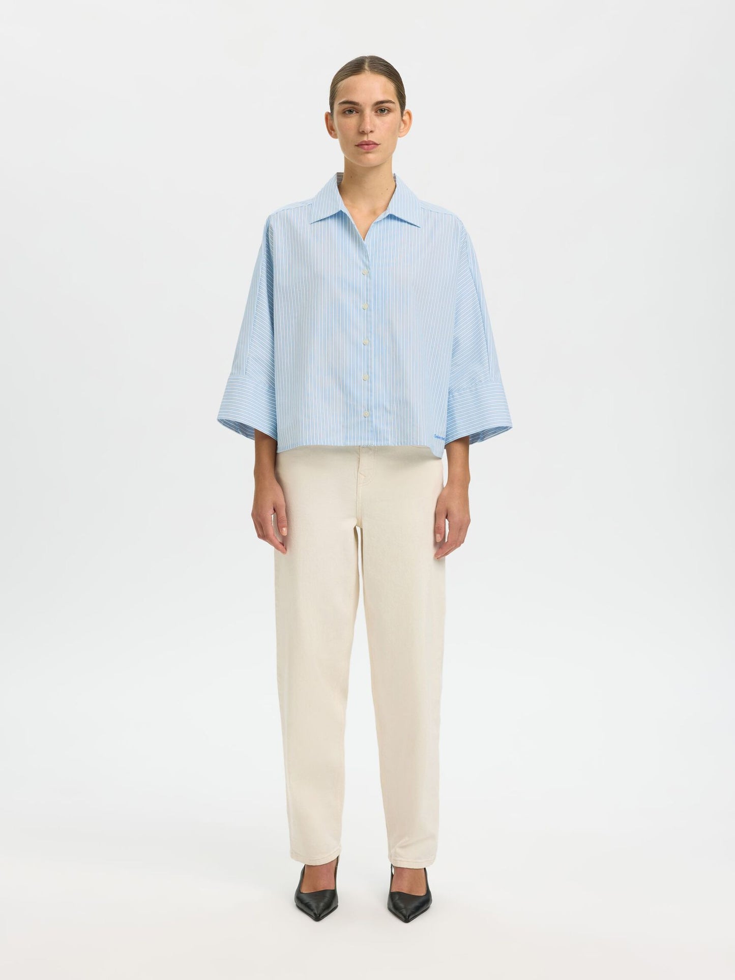 Person wearing a light blue shirt and beige pants on a white background