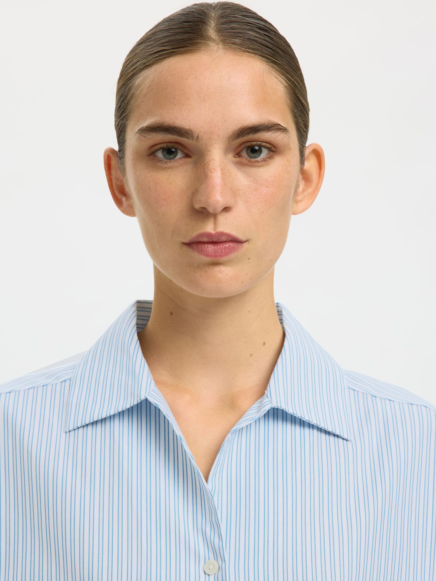 Person wearing a light blue striped shirt against a white background