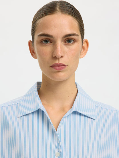Person wearing a light blue striped shirt against a white background