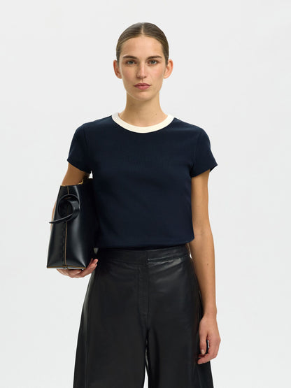 Woman holding a black handbag wearing a navy blue top and black leather pants on a white background