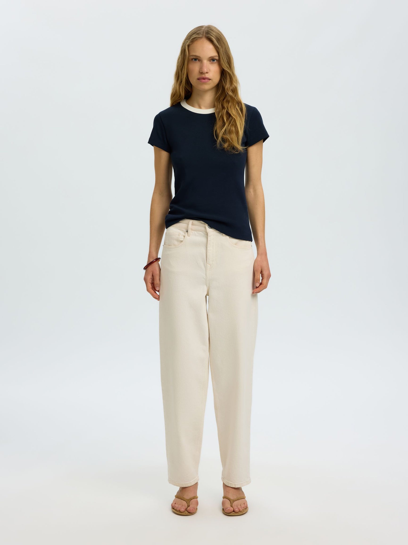 Woman wearing a navy t-shirt and beige pants on a white background