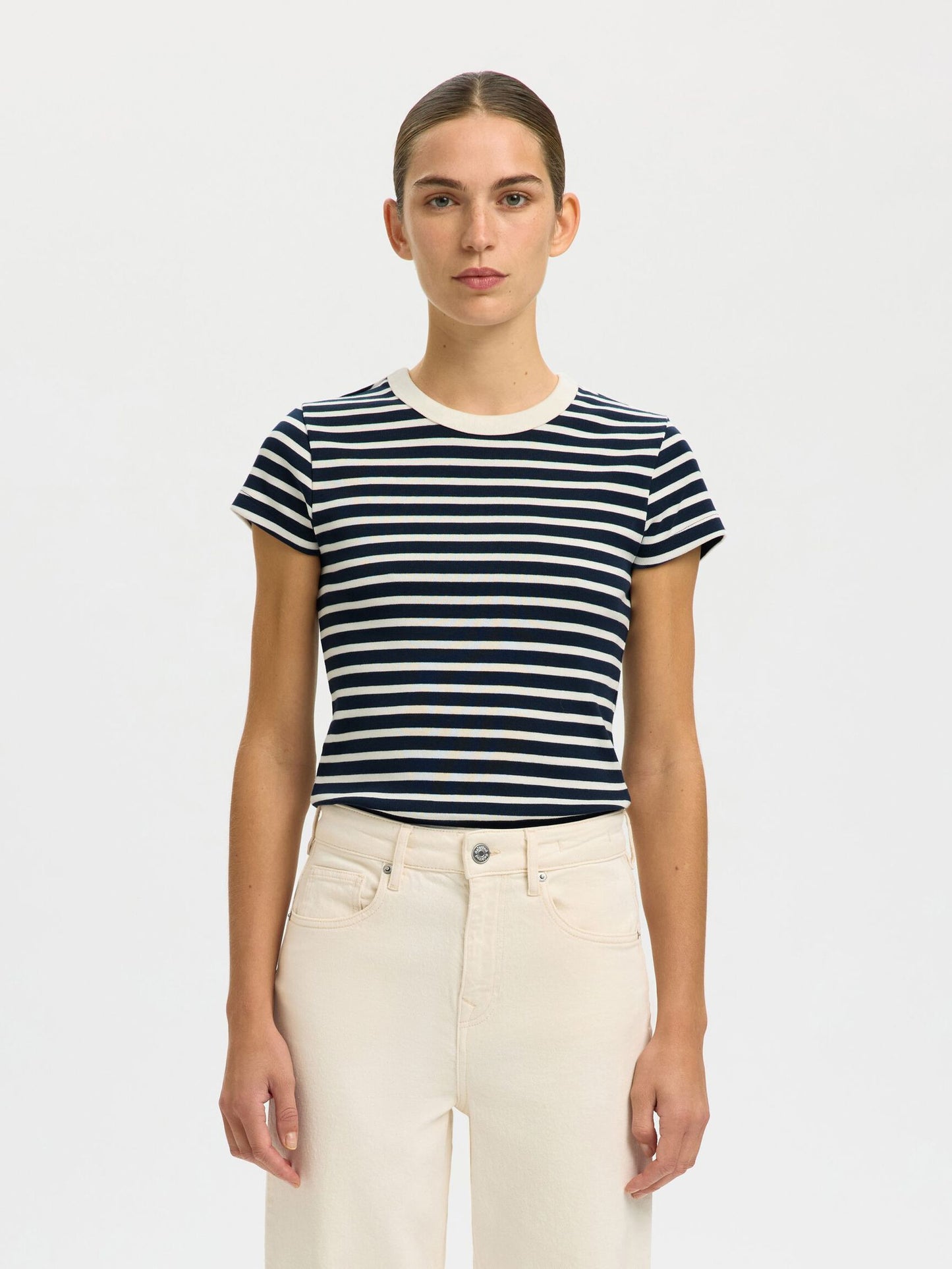 Woman wearing a navy and white striped t-shirt with beige pants on a plain background