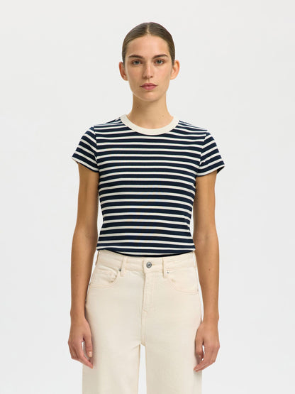 Woman wearing a navy and white striped t-shirt with beige pants on a plain background