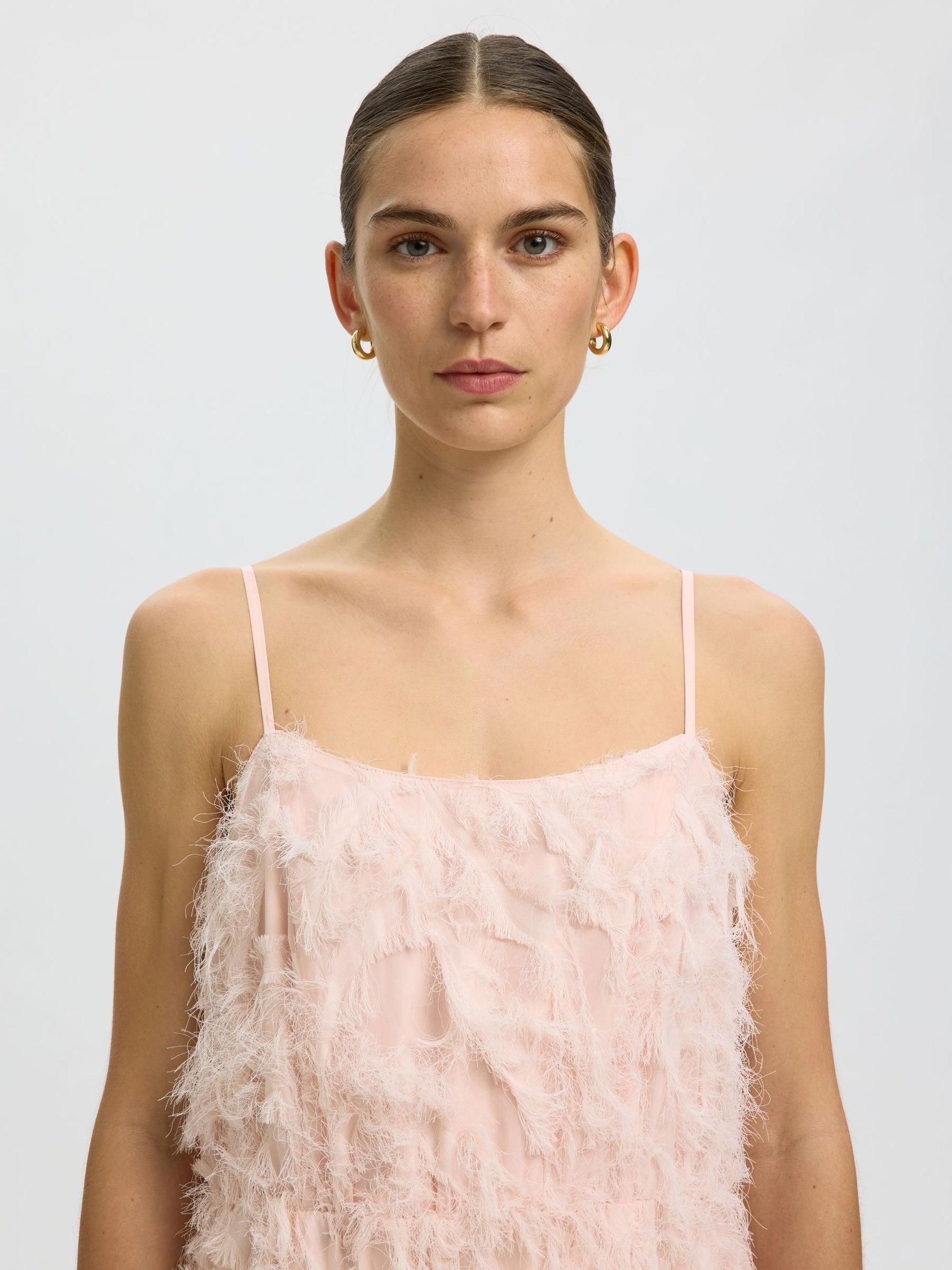 Woman wearing a light pink feathered dress against a plain background