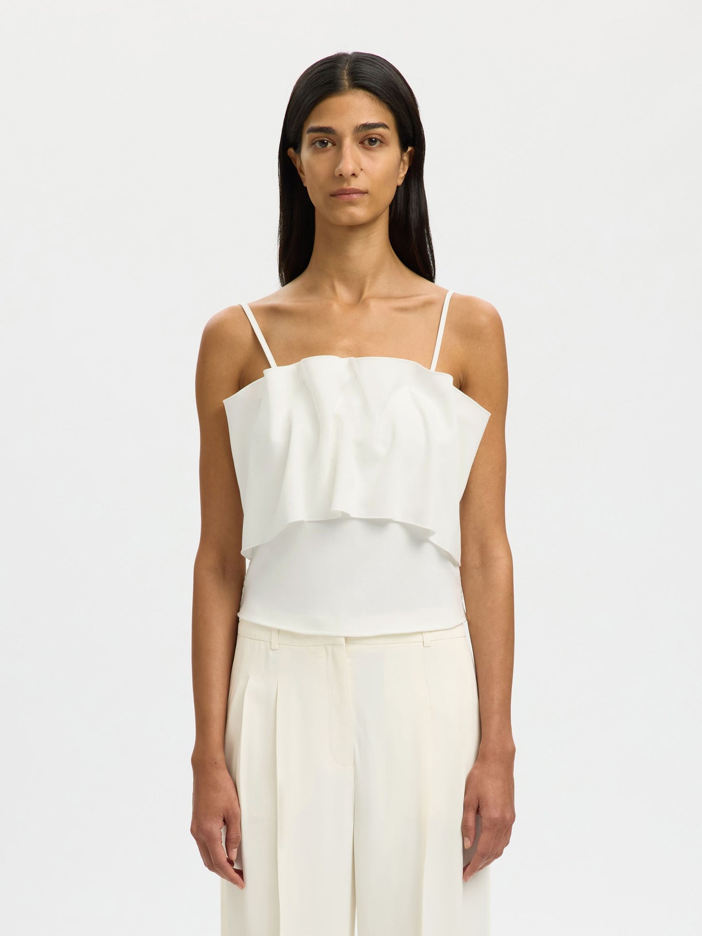 Woman wearing a white top and pants on a plain background