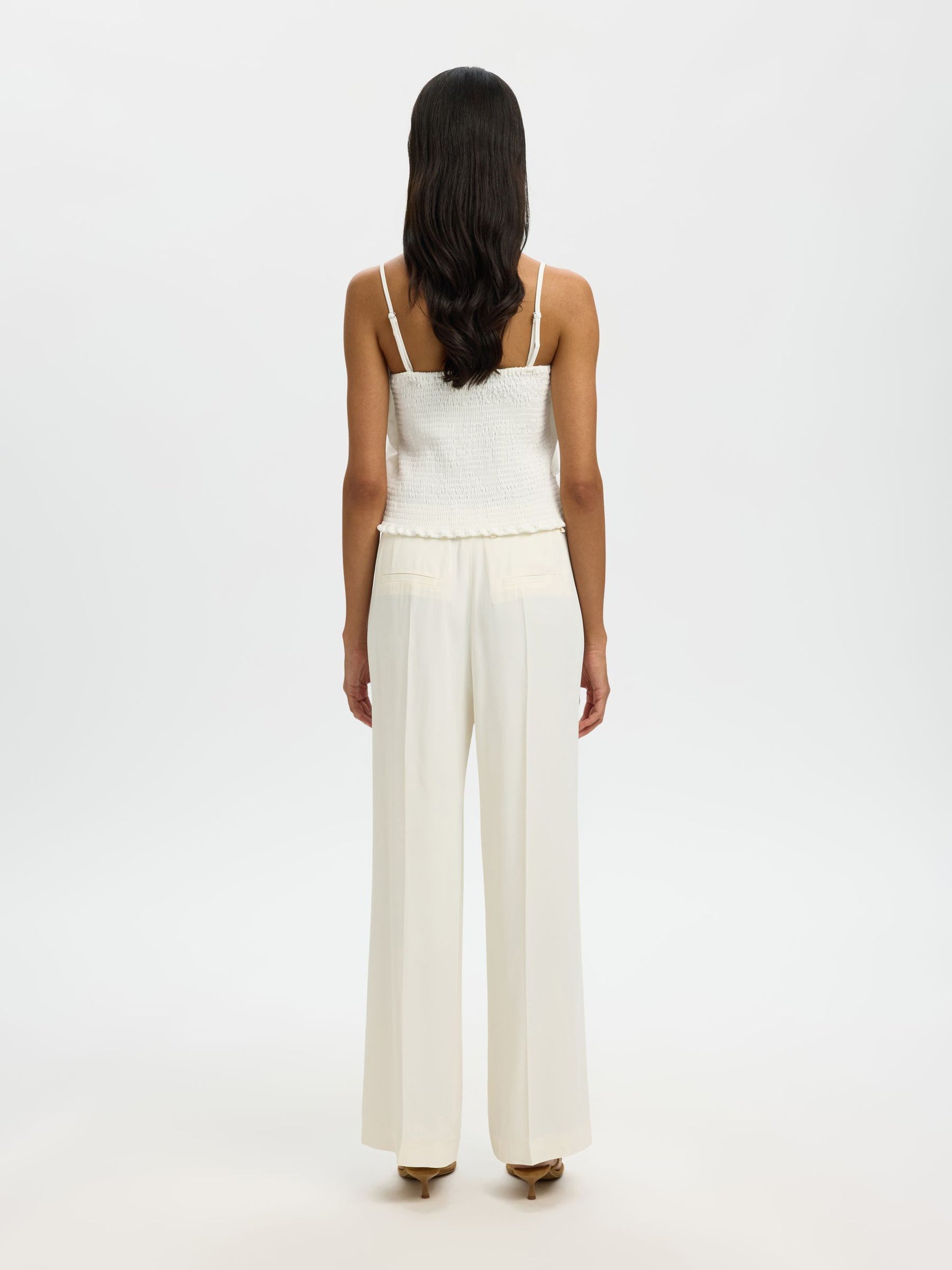 Woman wearing a white top and pants on a plain background