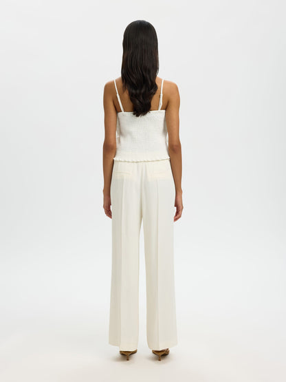Woman wearing a white top and pants on a plain background