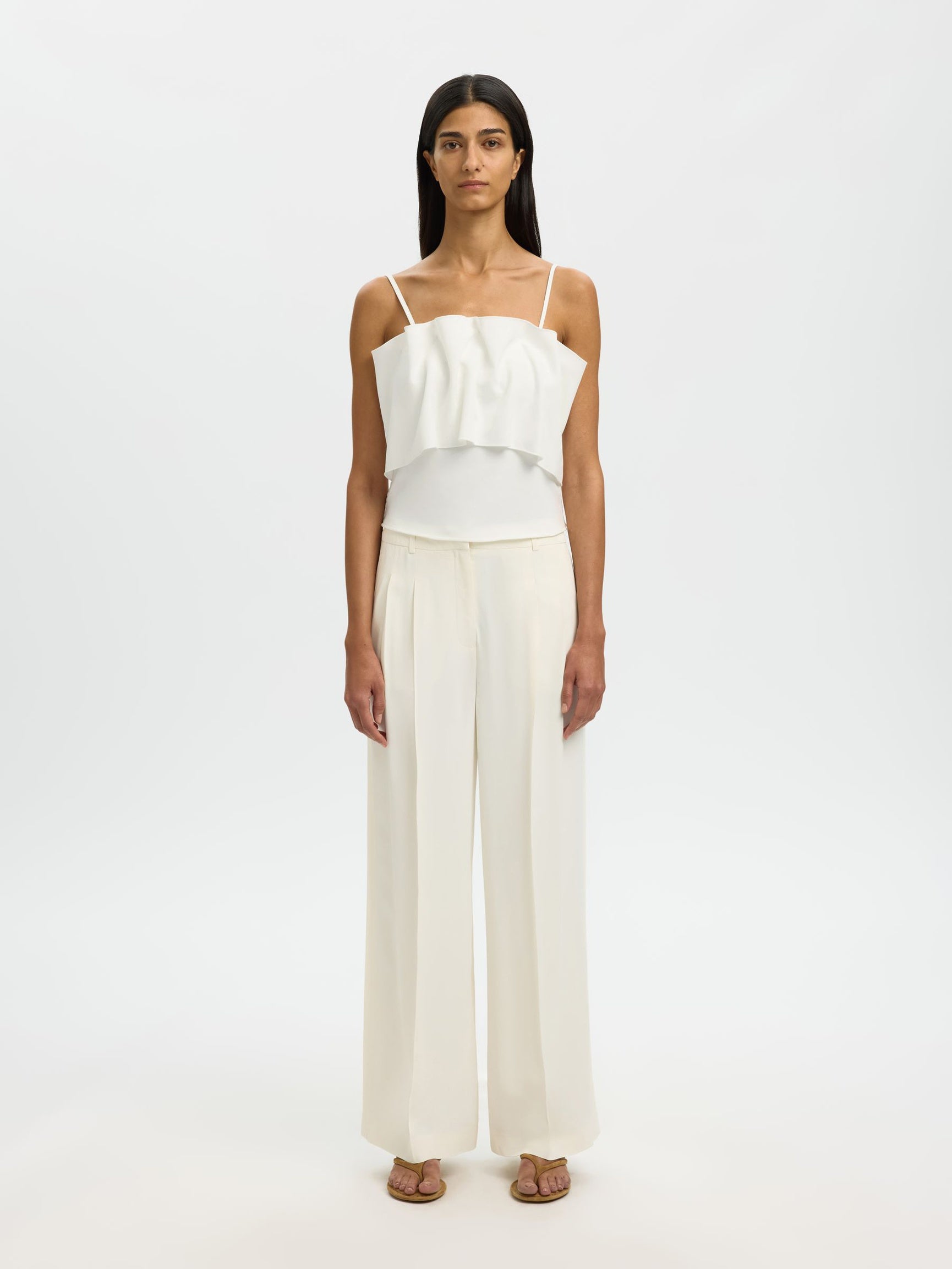 Woman wearing a white top and cream pants on a white background