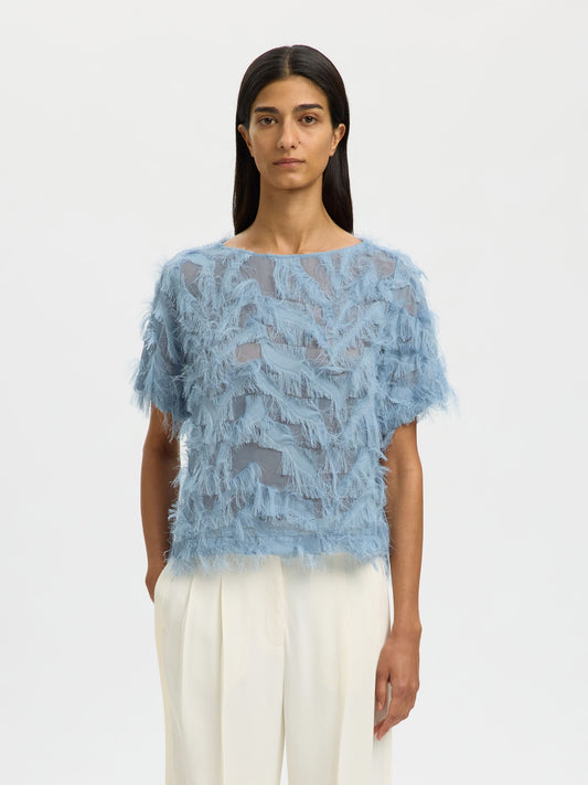 Woman wearing a blue lace top and white pants on a light gray background