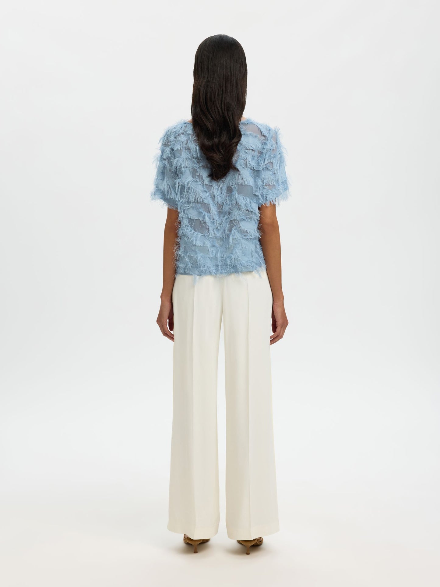 Woman wearing a blue patterned top and white pants on a white background