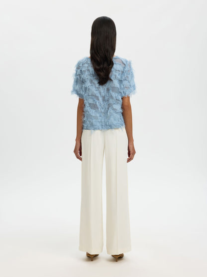 Woman wearing a blue patterned top and white pants on a white background