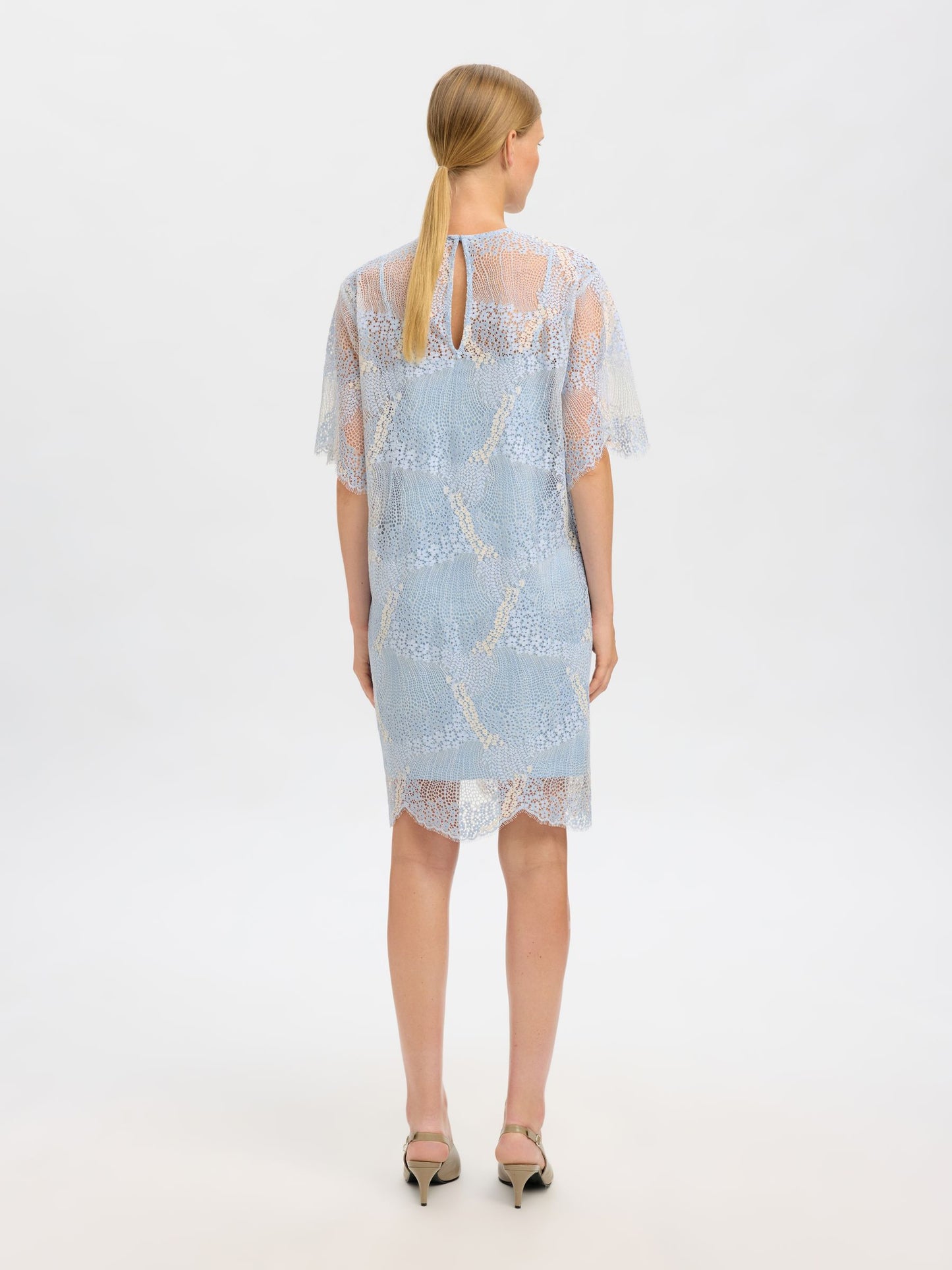 Woman wearing a light blue dress with lace details on a white background