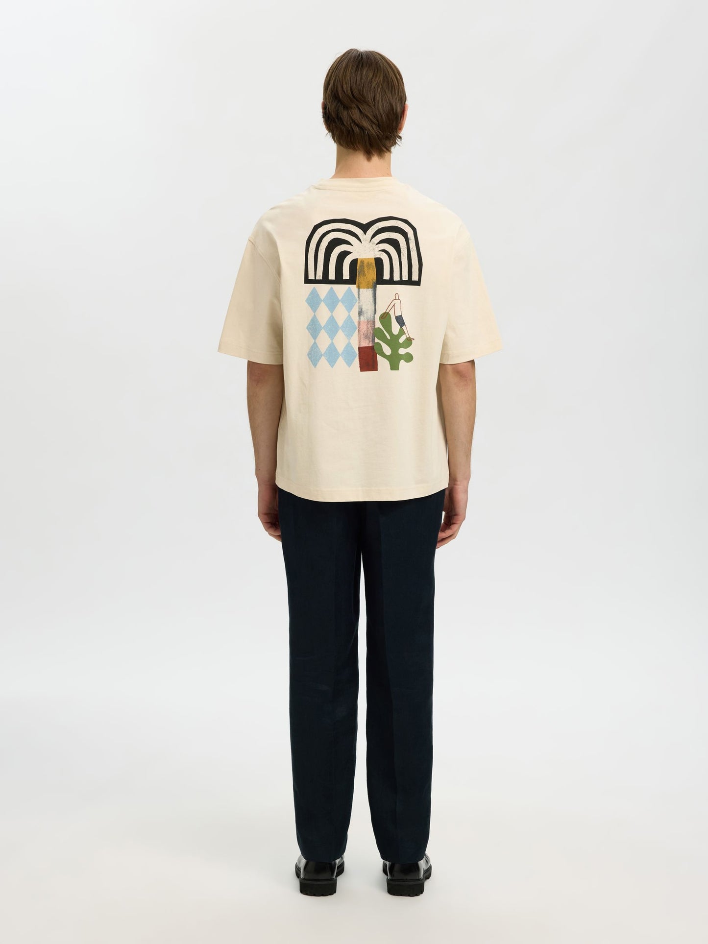 Person wearing a beige t-shirt with a colorful graphic on the back, standing against a white background