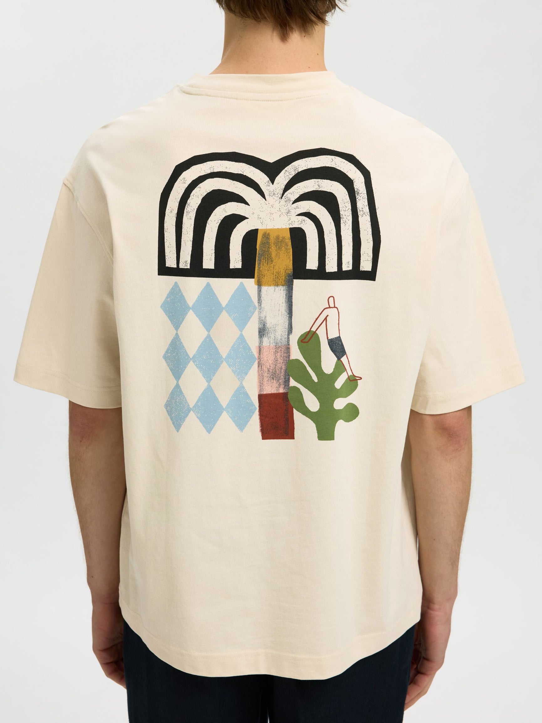 Person wearing a beige t-shirt with colorful graphic design on the back against a plain background