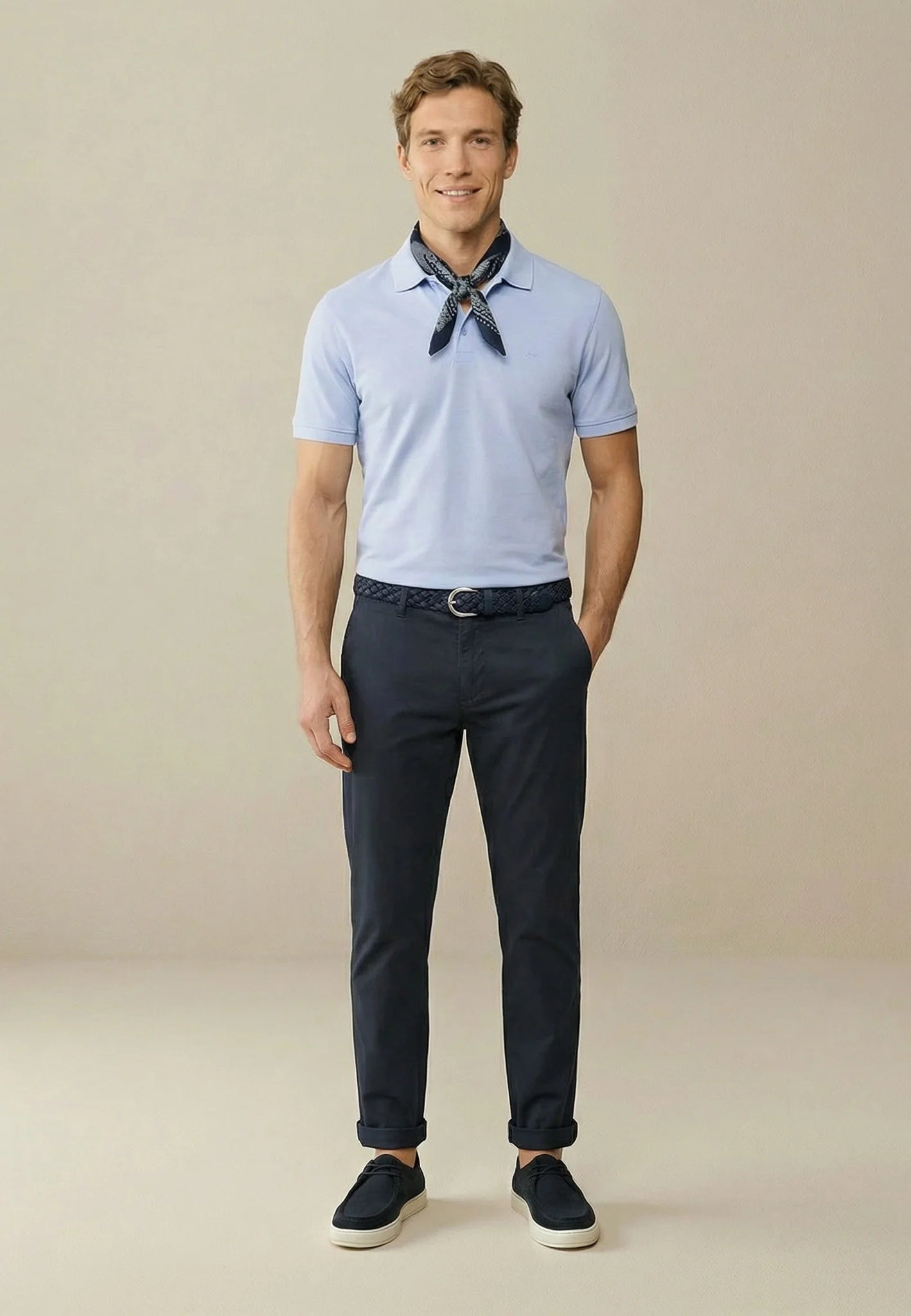 Man wearing a light blue polo shirt, dark pants, and black shoes on a beige background