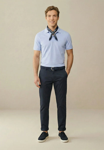 Man wearing a light blue polo shirt, dark pants, and black shoes on a beige background