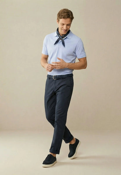 Man wearing a light blue polo shirt, dark pants, and black shoes on a beige background