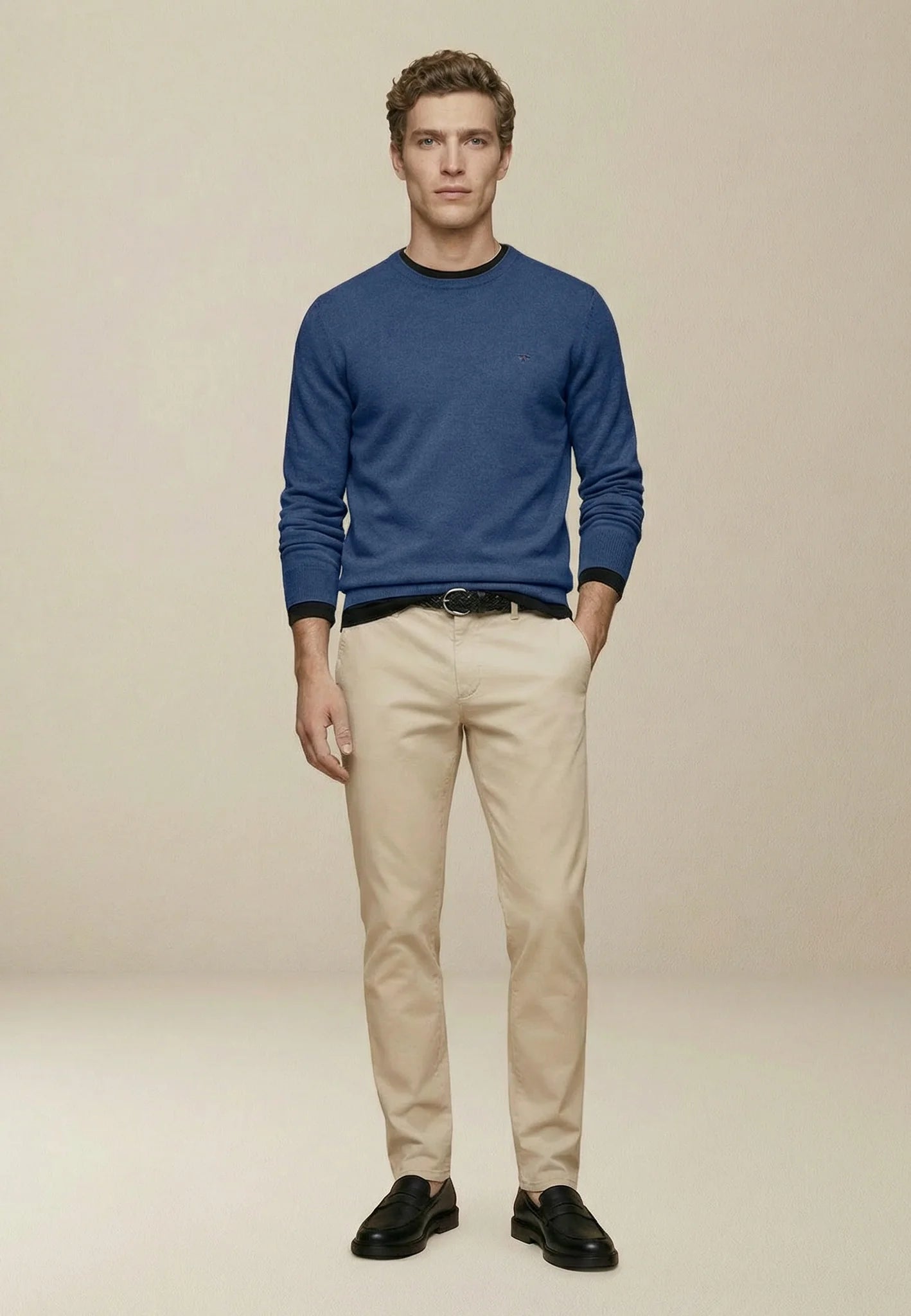 Man wearing a blue sweater, beige pants, and black shoes on a beige background