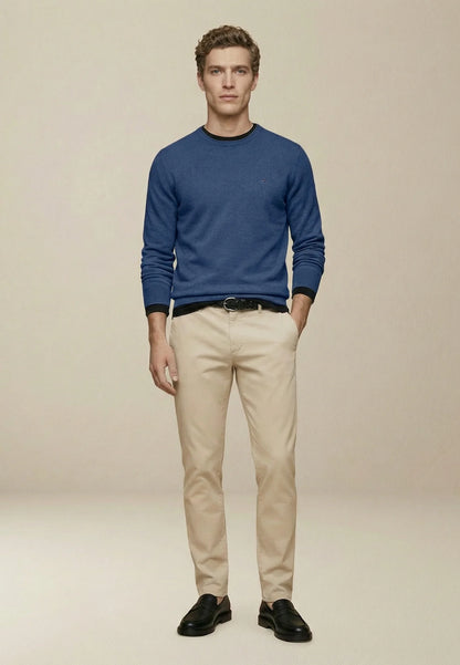 Man wearing a blue sweater, beige pants, and black shoes on a beige background