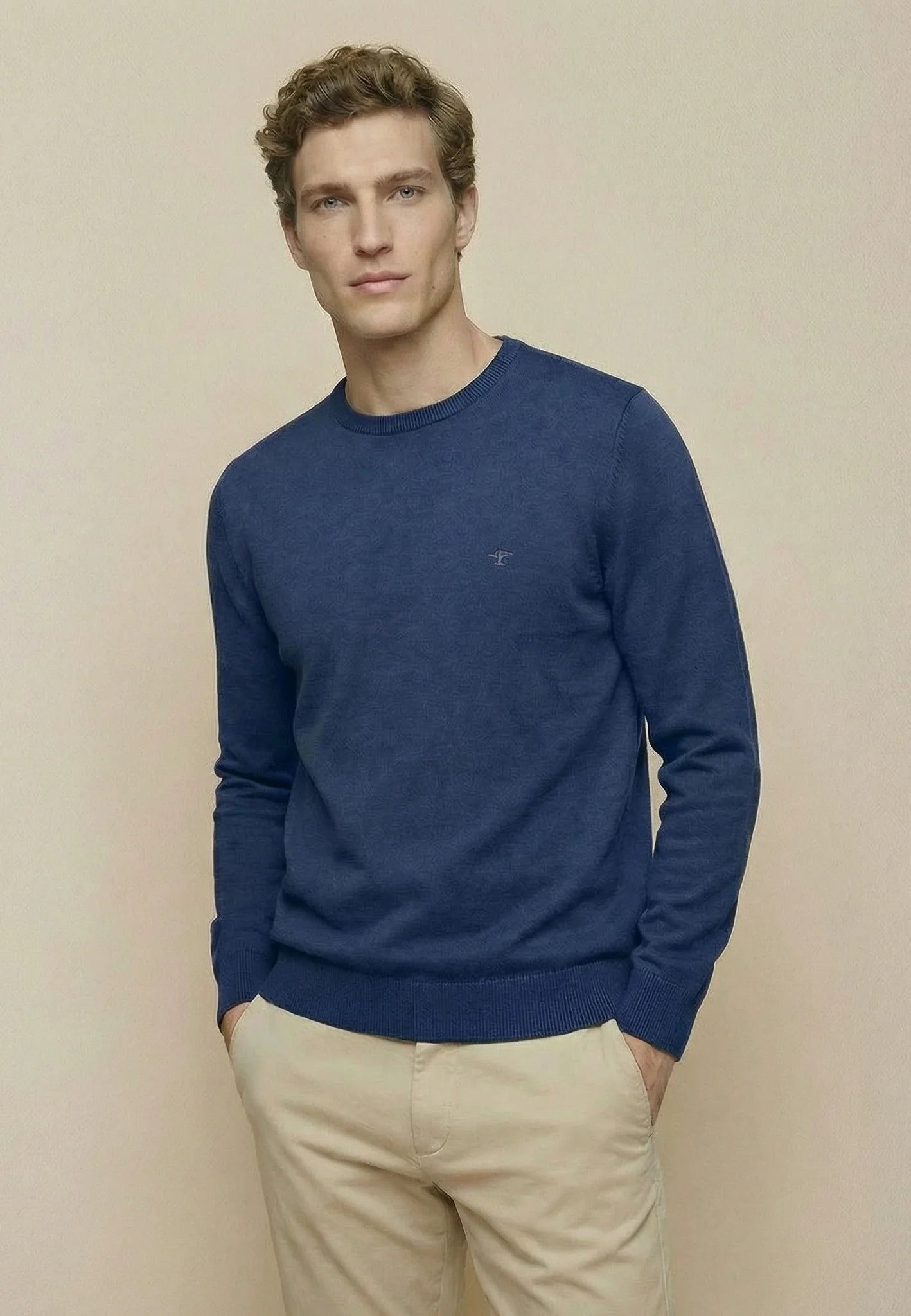 Man wearing a blue sweater and beige pants against a beige background
