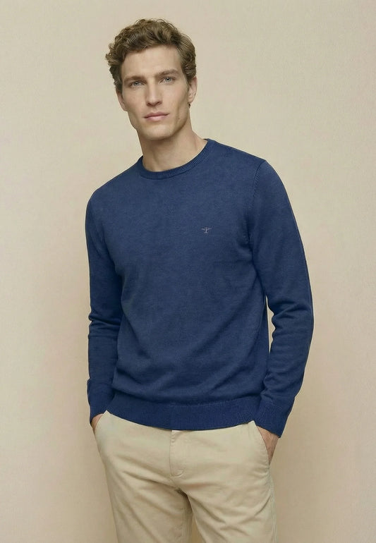 Man wearing a blue sweater and beige pants against a beige background