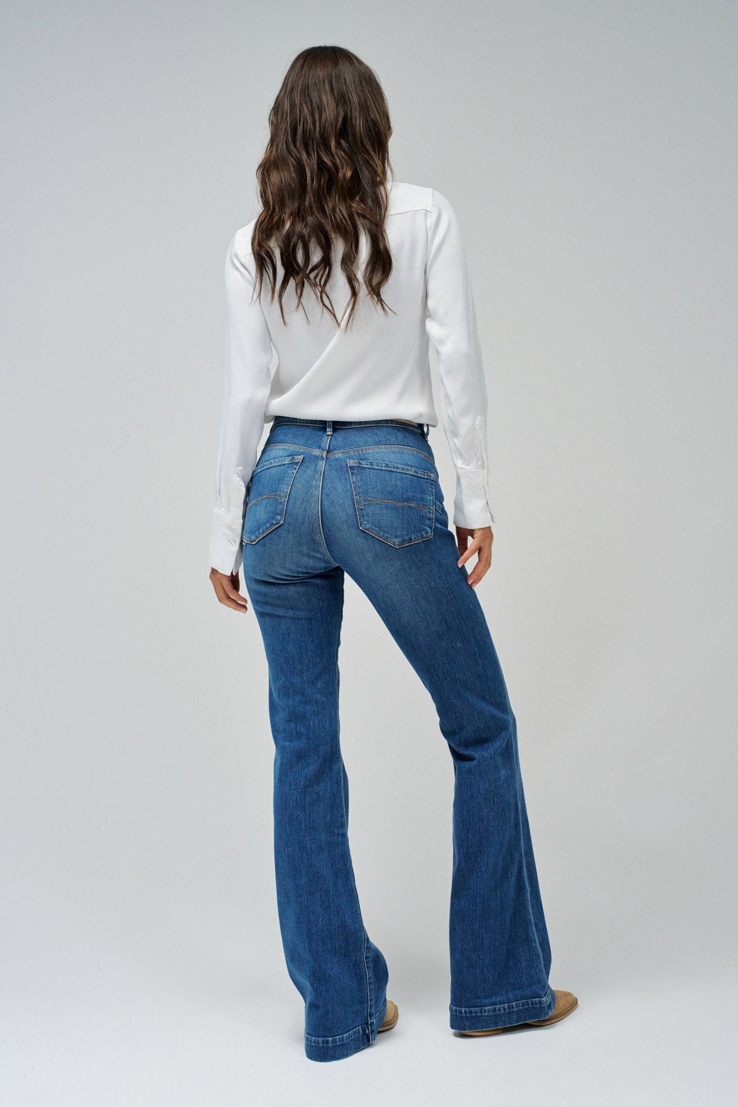 Person wearing blue flared jeans and a white shirt on a gray background