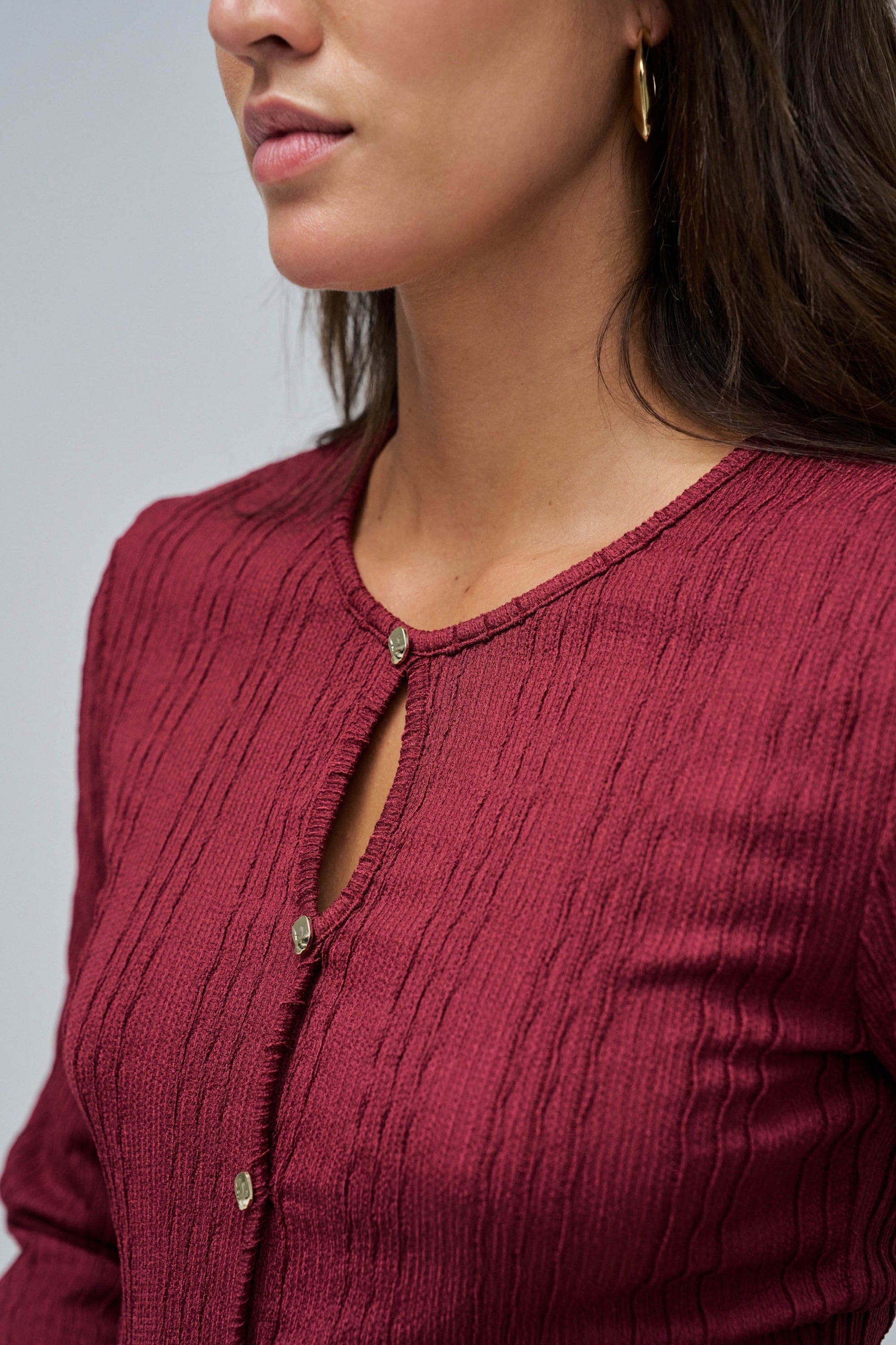 Close-up of a person wearing a burgundy textured cardigan on a plain background