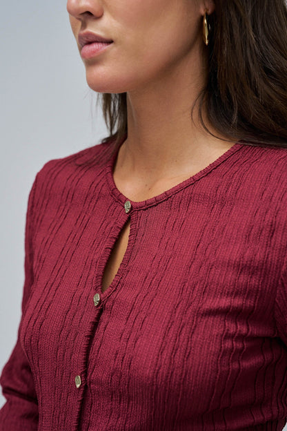 Close-up of a person wearing a burgundy textured cardigan on a plain background