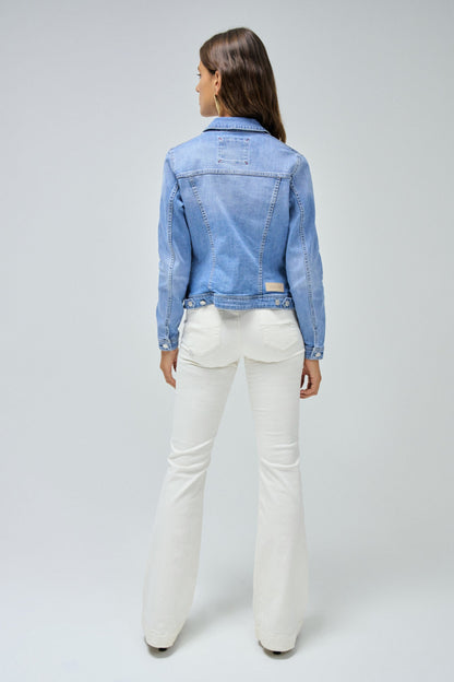 Woman wearing a light blue denim jacket and white pants on a gray background