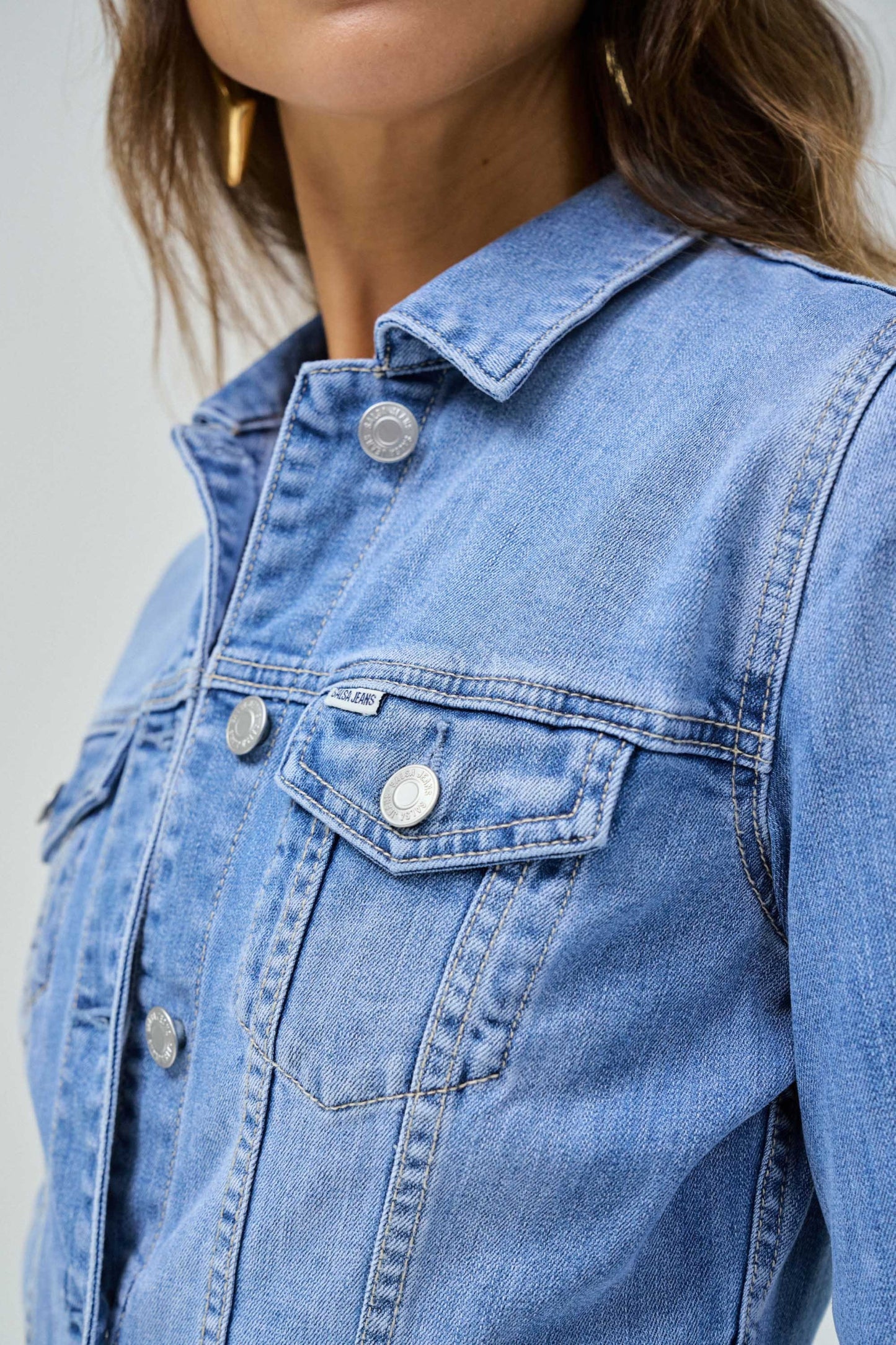 Close-up of a blue denim jacket with button details on a plain background