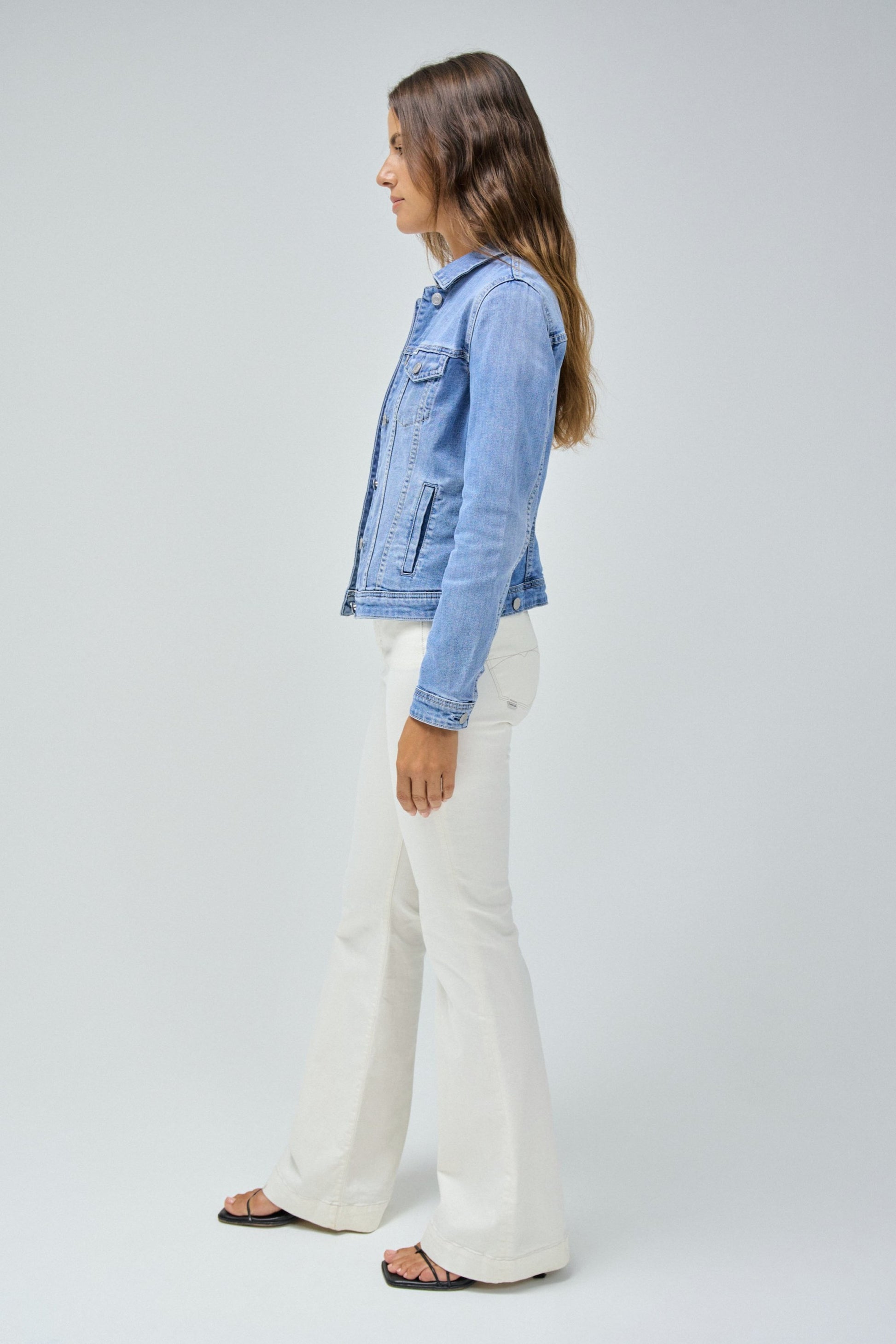 Woman wearing a denim jacket and white pants on a plain background